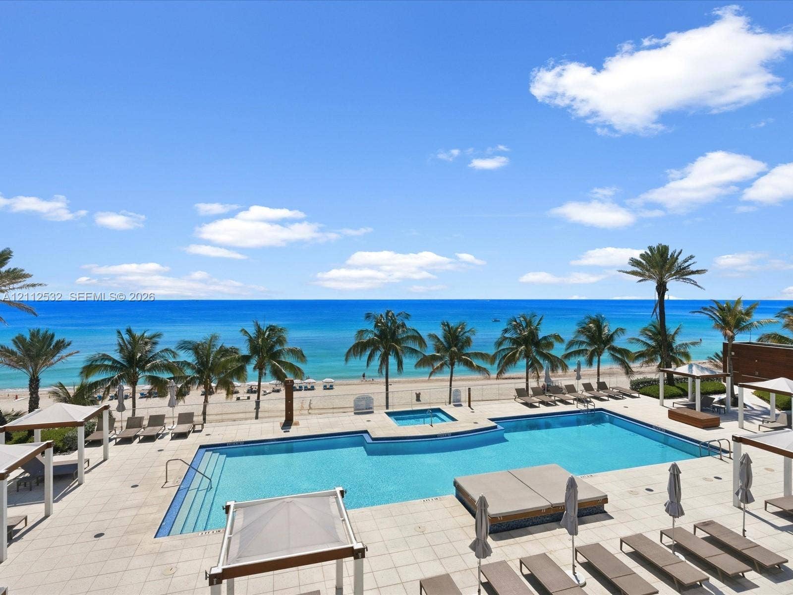18911 Collins Avenue, #601, Sunny Isles Beach, FL 33160 Swimming pool featuring a built-in spa, expansive stone-paver decking, and coastal horizon backdrop