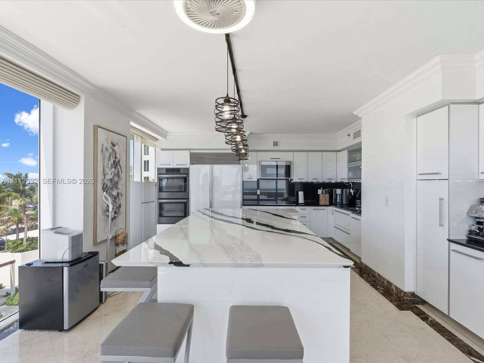 18911 Collins Avenue, #601, Sunny Isles Beach, FL 33160 Kitchen featuring a substantial waterfall-edge island with stone countertop, flat-panel white cabinetry, built-in stainless steel appliances, multi-pendant track lighting, and light-toned tile flooring