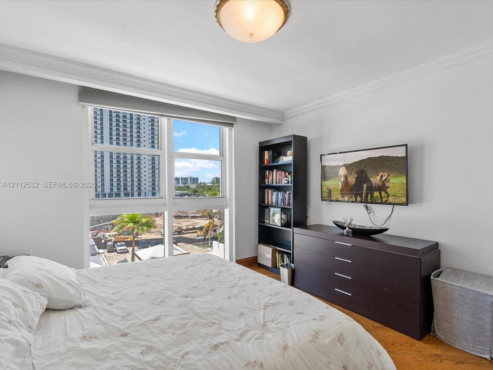 18911 Collins Avenue, #601, Sunny Isles Beach, FL 33160 Wood-finish flooring, crown molding, and a dual-pane window featuring a neutral-toned roller shade