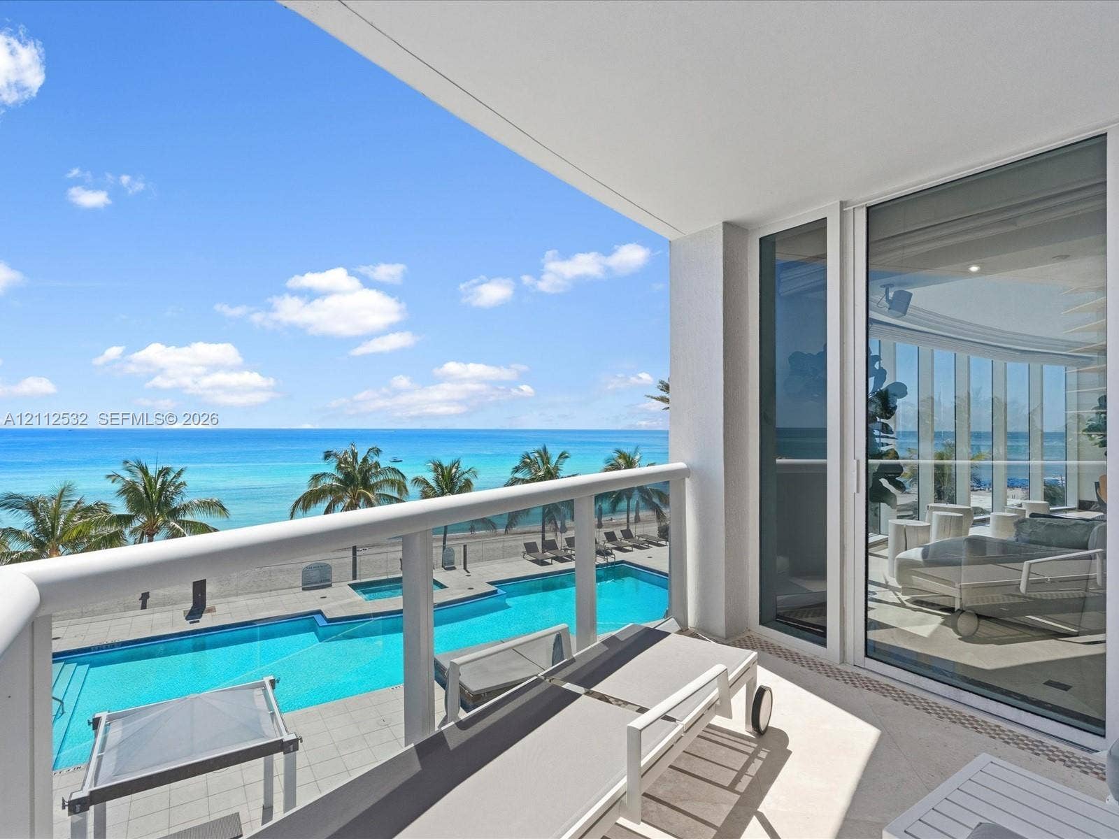 18911 Collins Avenue, #601, Sunny Isles Beach, FL 33160 Covered balcony with glass and metal railings, overlooking a swimming pool and ocean backdrop, featuring floor-to-ceiling sliding glass doors