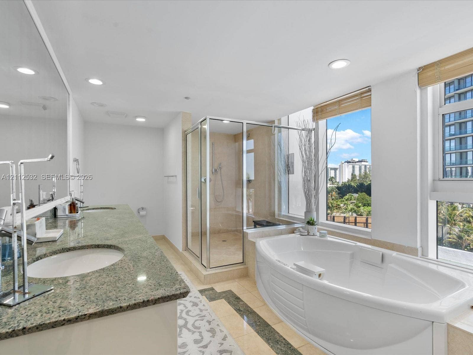 18911 Collins Avenue, #601, Sunny Isles Beach, FL 33160 Dual-sink vanity with natural stone countertop, corner glass-enclosed shower, deep soaking tub, tile flooring with stone inlay, and large windows with integrated blinds