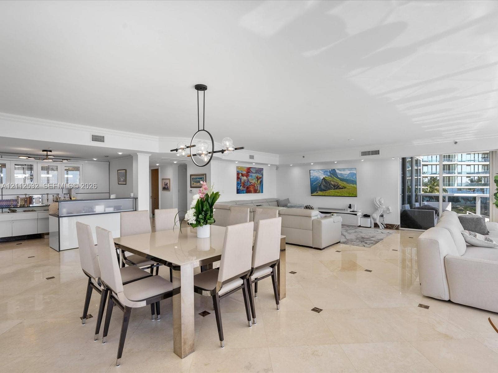 18911 Collins Avenue, #601, Sunny Isles Beach, FL 33160 Open-concept interior featuring light-toned stone tile flooring with decorative inserts, floor-to-ceiling glass panel doors, modern geometric multi-light chandelier, and high-gloss white cabinetry