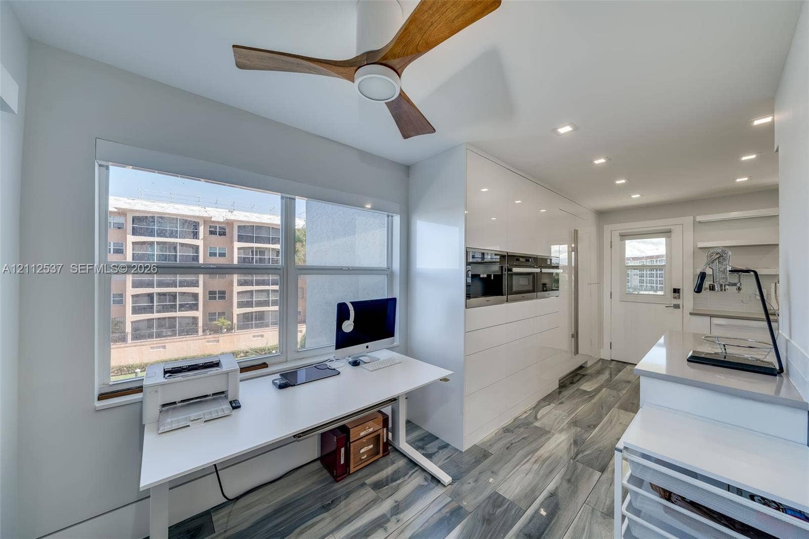 2871 N Ocean Boulevard, #R360, Boca Raton, FL 33431 Modern kitchen featuring high-gloss white cabinetry, integrated stainless steel appliances, wood-finish ceiling fan, recessed lighting, and large-format gray patterned flooring