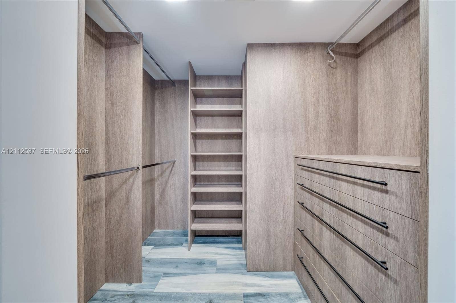 2871 N Ocean Boulevard, #R360, Boca Raton, FL 33431 Walk-in closet featuring custom wood-finish cabinetry, floor-to-ceiling shelving, built-in dresser drawers, matte black hardware, and wood-finish flooring