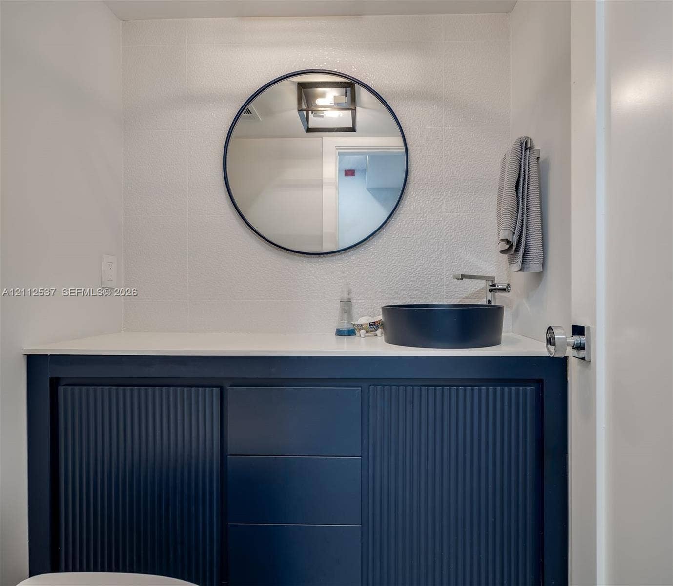 2871 N Ocean Boulevard, #R360, Boca Raton, FL 33431 Navy blue fluted vanity with a white countertop, round black-framed mirror, and matte black vessel sink