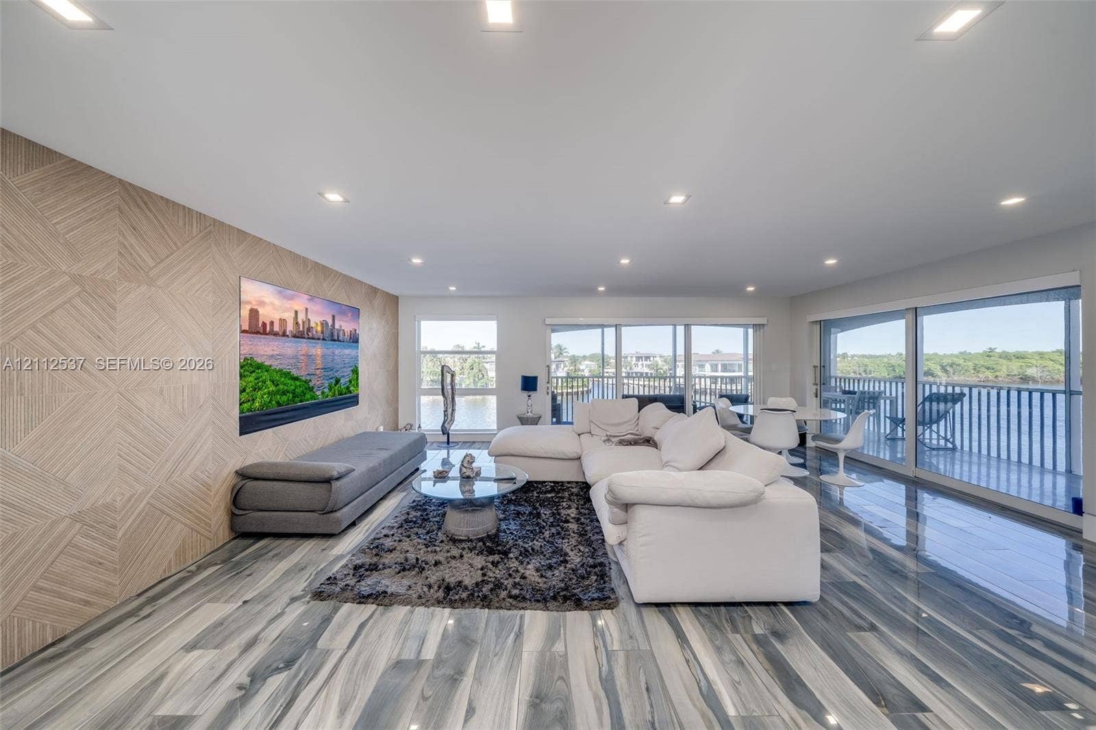2871 N Ocean Boulevard, #R360, Boca Raton, FL 33431 Expansive living space featuring wood-finish flooring, a textured wood-panel accent wall, recessed lighting, and floor-to-ceiling glass sliding doors