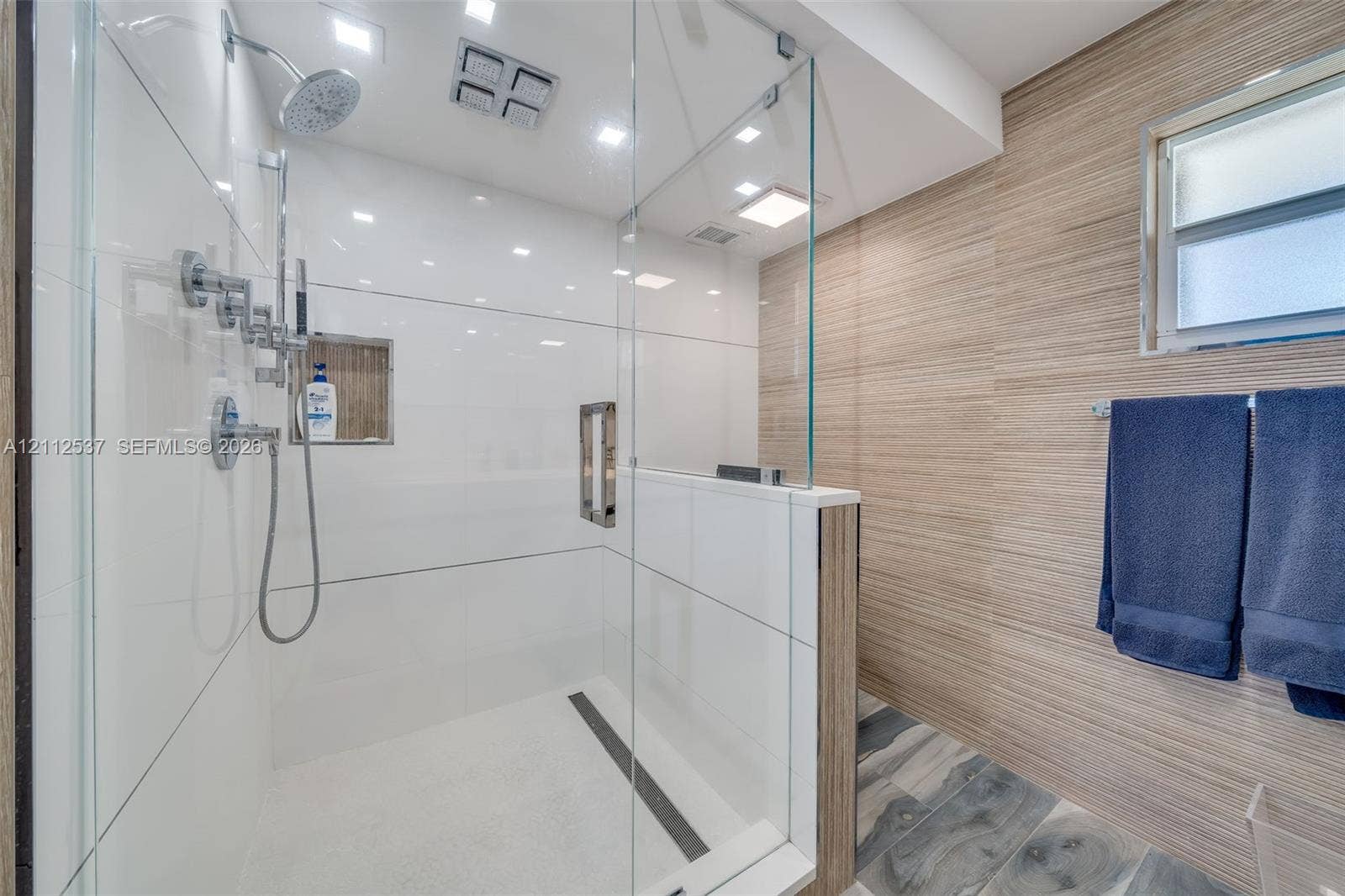 2871 N Ocean Boulevard, #R360, Boca Raton, FL 33431 Walk-in shower featuring a glass enclosure, rainfall showerhead, handheld sprayer, built-in recessed wall niche, and wood-finish wall tile
