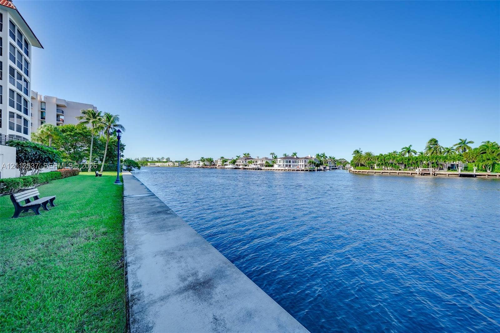 2871 N Ocean Boulevard, #R360, Boca Raton, FL 33431 Waterfront property featuring a concrete seawall, manicured lawn, and mature palm trees