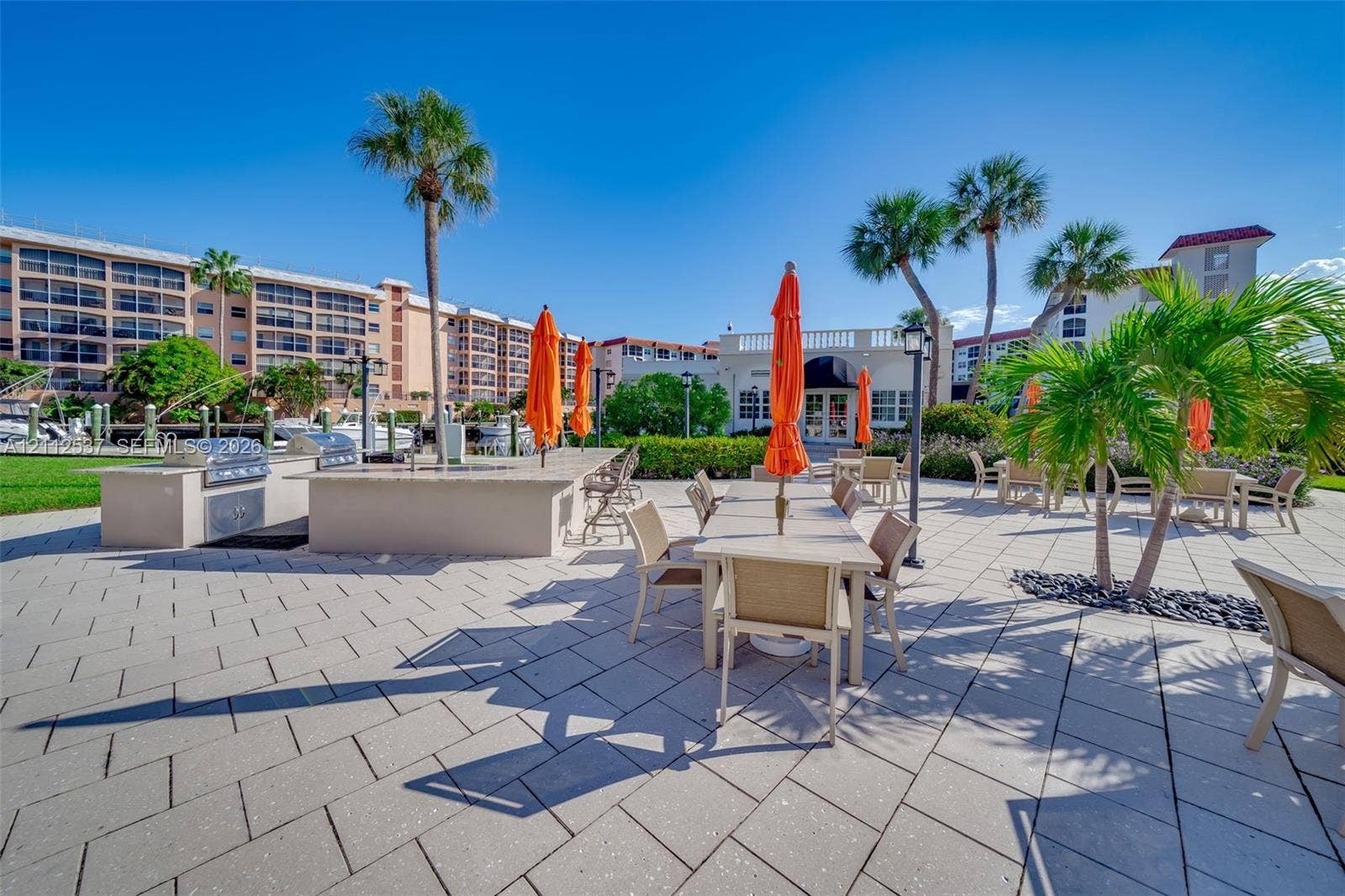 2871 N Ocean Boulevard, #R360, Boca Raton, FL 33431 Outdoor patio area featuring stone-paver flooring, a built-in outdoor kitchen with stainless steel appliances, and mature palm trees