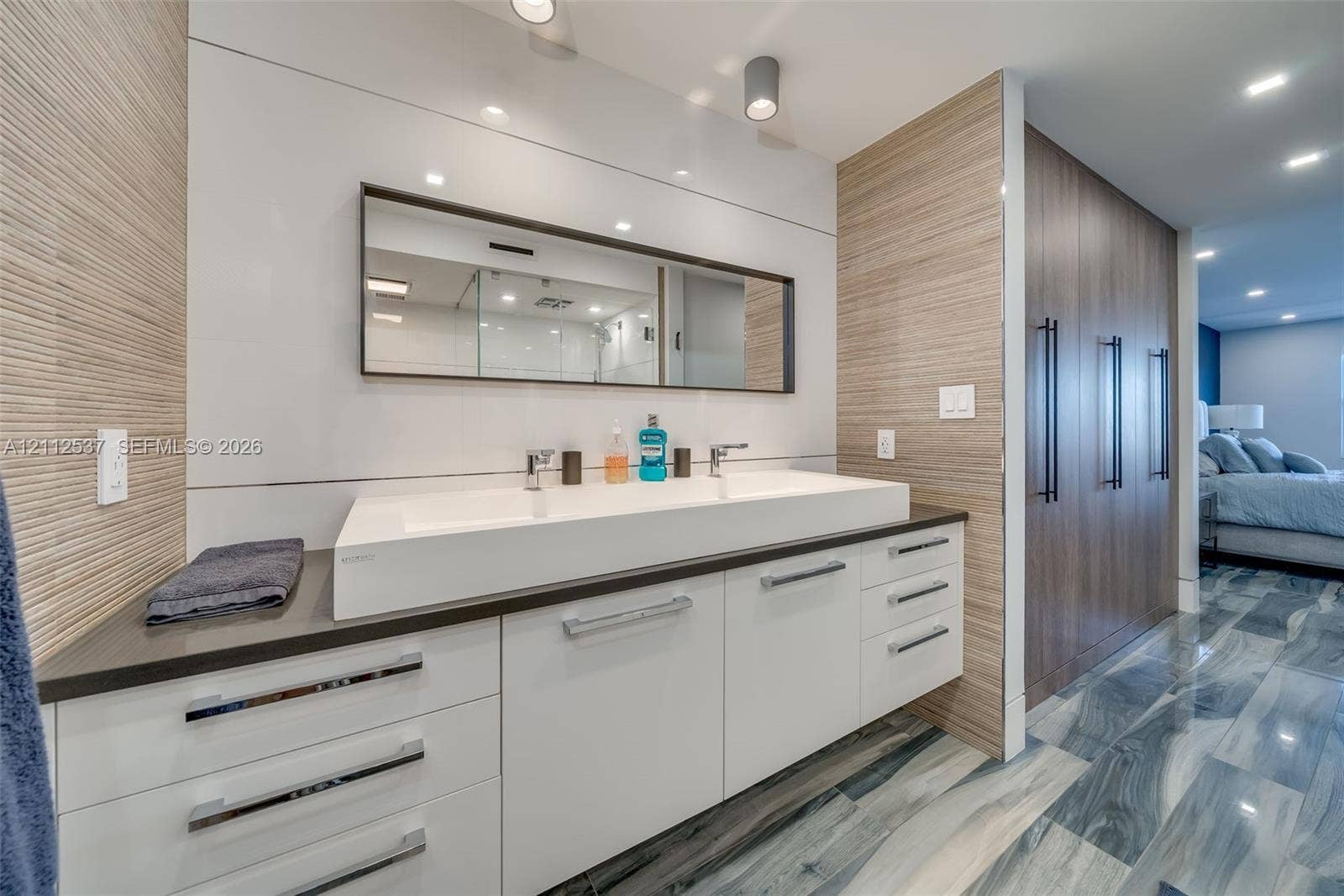 2871 N Ocean Boulevard, #R360, Boca Raton, FL 33431 Modern floating vanity featuring a wide rectangular double-basin sink, high-gloss white cabinetry, integrated drawer pulls, wood-finish wall paneling, and recessed ceiling lighting