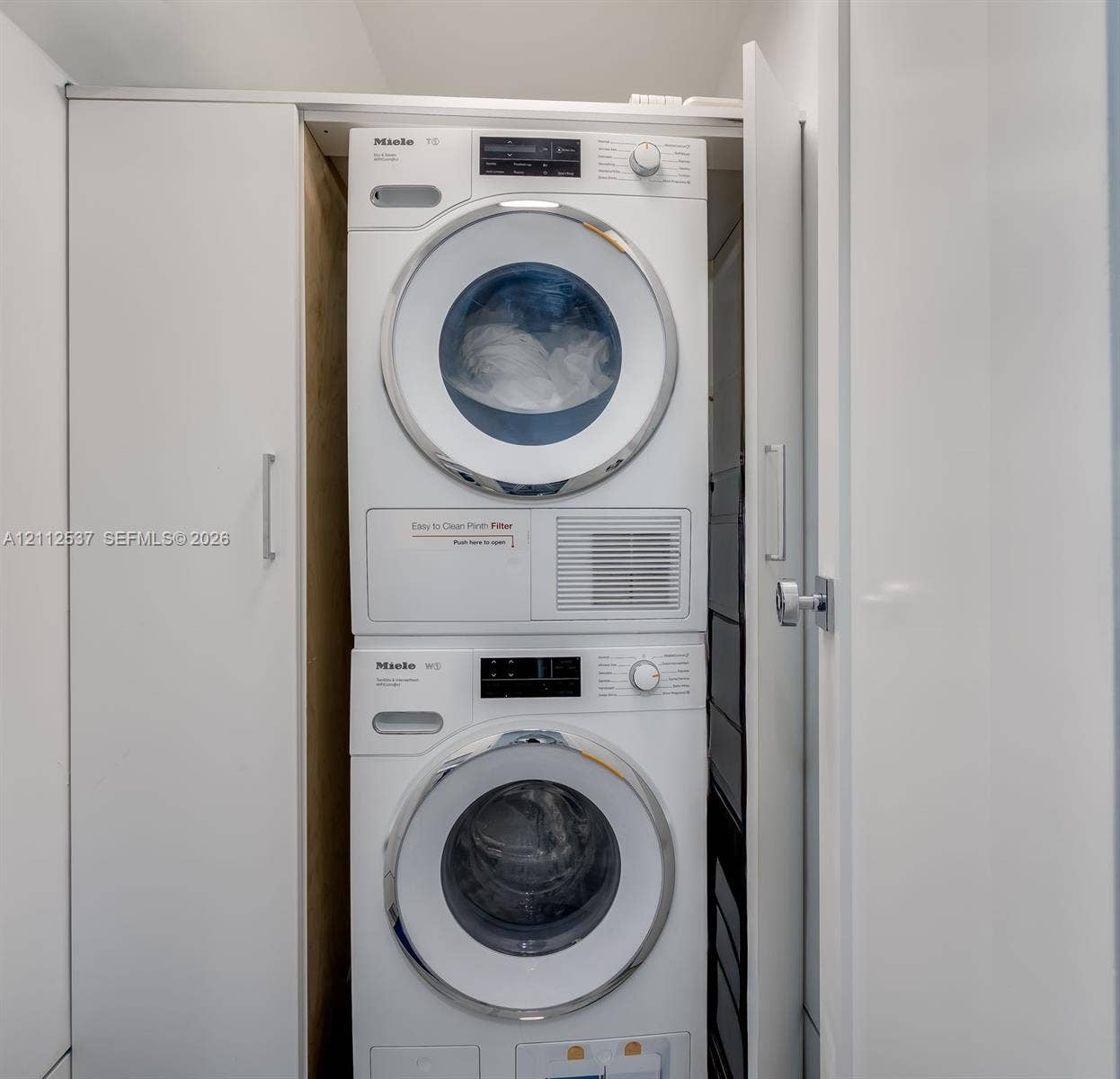 2871 N Ocean Boulevard, #R360, Boca Raton, FL 33431 Stackable Miele washer and dryer set enclosed within custom white cabinetry featuring minimalist hardware
