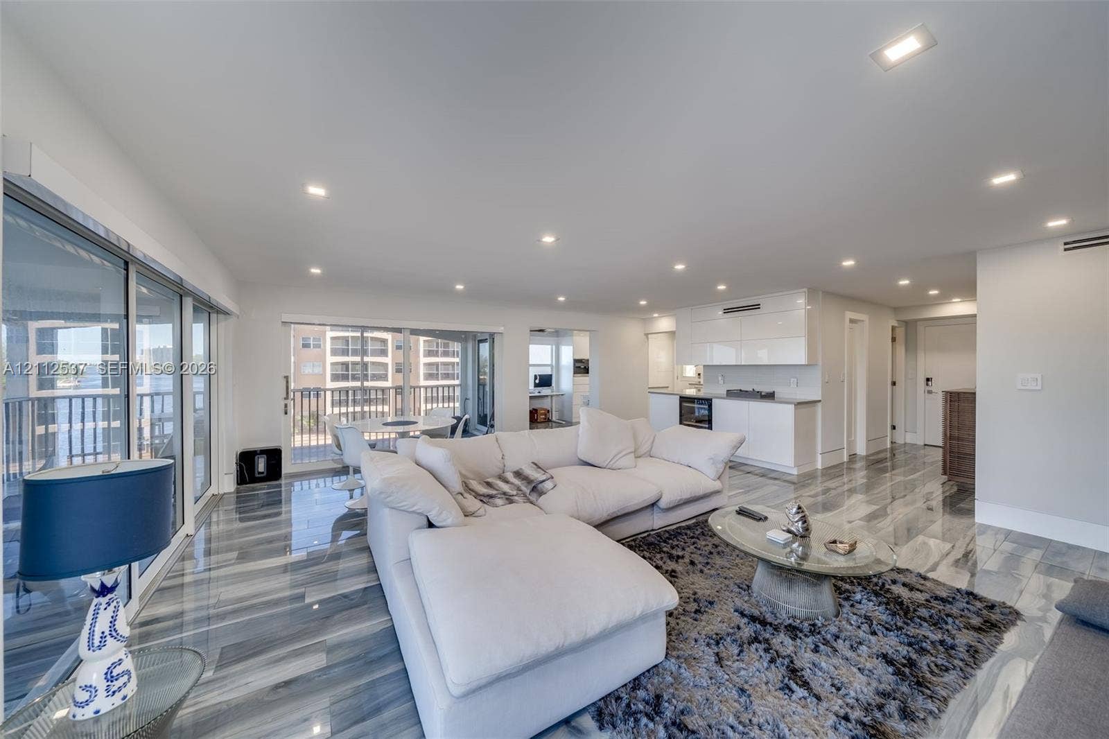 2871 N Ocean Boulevard, #R360, Boca Raton, FL 33431 Open-concept living space featuring high-gloss stone flooring, recessed ceiling lighting, sliding glass door access to an exterior balcony, and white cabinetry