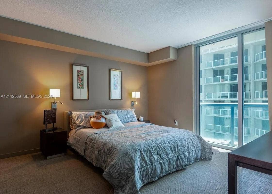 17315 Collins Avenue, #705, Sunny Isles Beach, FL 33160 Floor-to-ceiling glass sliding doors, wall-mounted adjustable bedside lighting, and neutral-toned wall paint