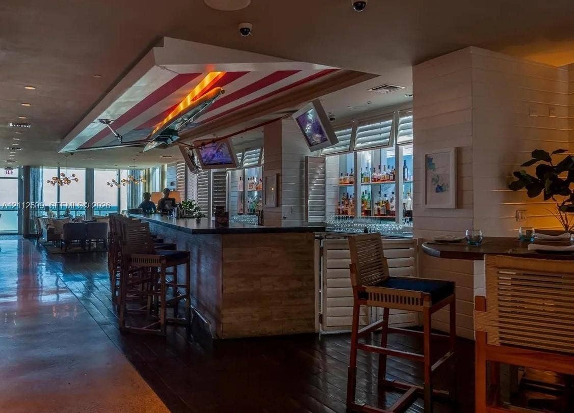 17315 Collins Avenue, #705, Sunny Isles Beach, FL 33160 Custom bar featuring dark wood-finish flooring, built-in shelving with integrated lighting, wood-paneled counter, and louvered shutters