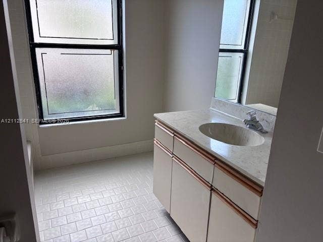Bathroom featuring a vanity with stone-finish countertop, integrated oval basin, light-toned cabinetry, and tiled flooring