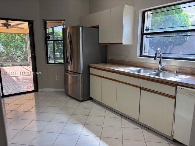 Kitchen featuring stainless steel refrigerator, white cabinetry, neutral tile flooring, dual-basin stainless steel sink with gooseneck faucet, and exterior access via sliding glass door