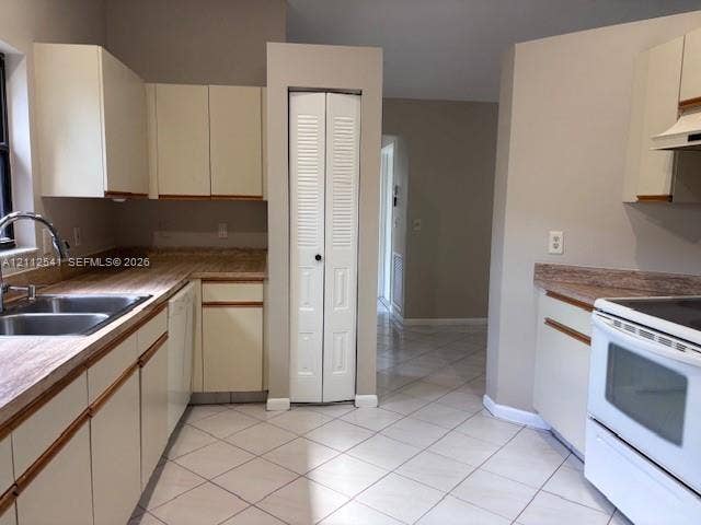 Kitchen featuring light-toned cabinetry, laminate countertops, a stainless steel double-basin sink, tile flooring, and a built-in pantry with bi-fold doors