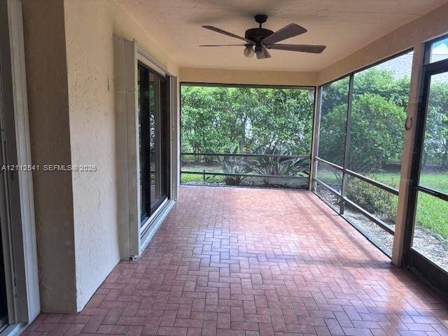 Screened lanai featuring herringbone-patterned tile flooring, a ceiling fan, and sliding glass door access
