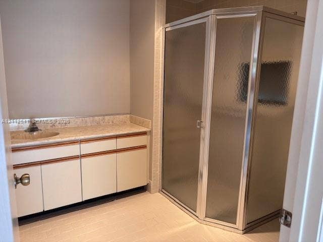 Bathroom featuring a stone-surface vanity with an integrated sink, white cabinetry with wood trim, a corner shower enclosure with textured glass doors, and tiled flooring