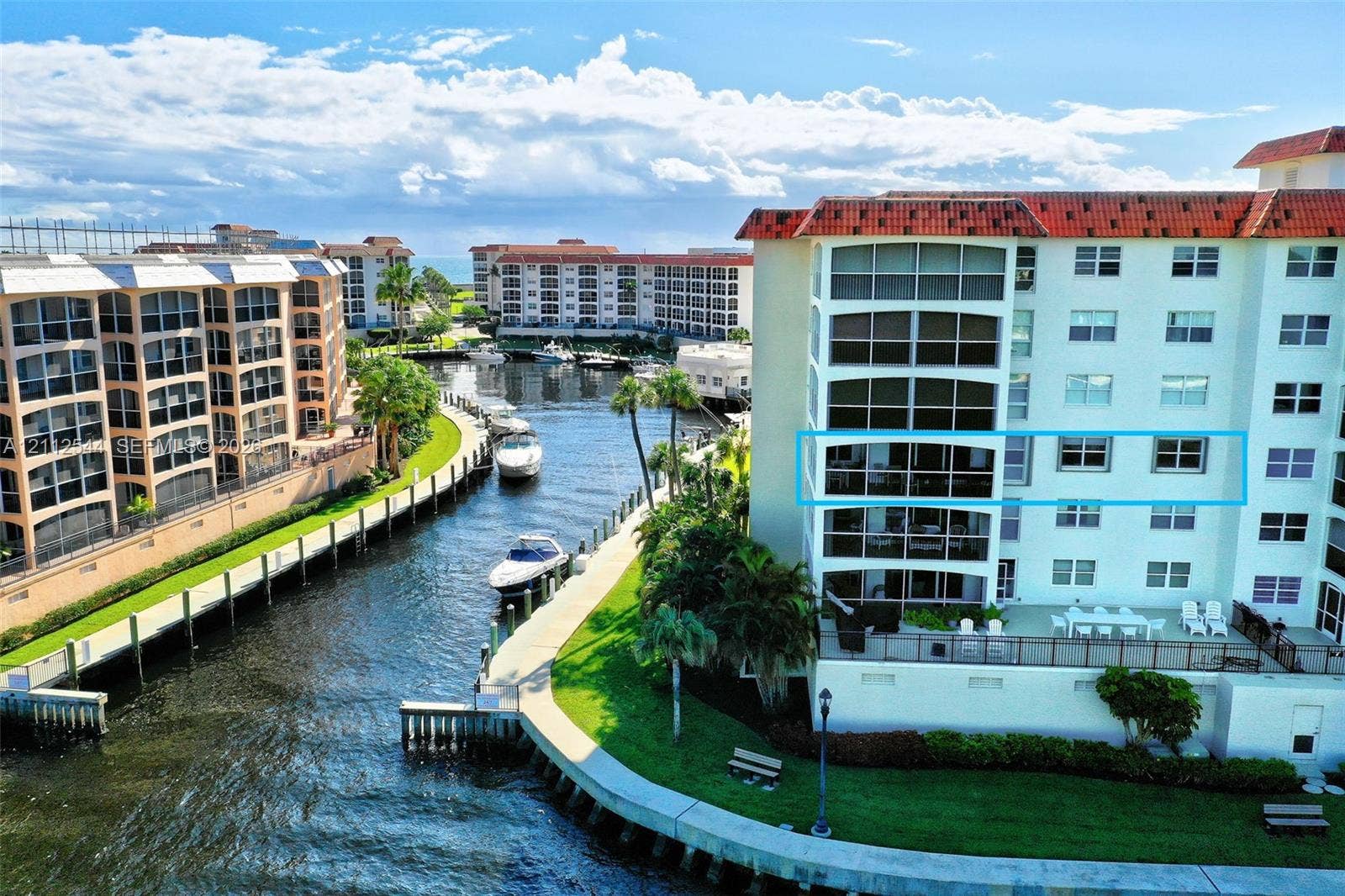 2871 N Ocean Boulevard, #R360, Boca Raton, Boca Raton, FL 33431 Multi-story waterfront residential building featuring a tile roof, expansive glass-enclosed balconies, and a concrete bulkhead along the canal