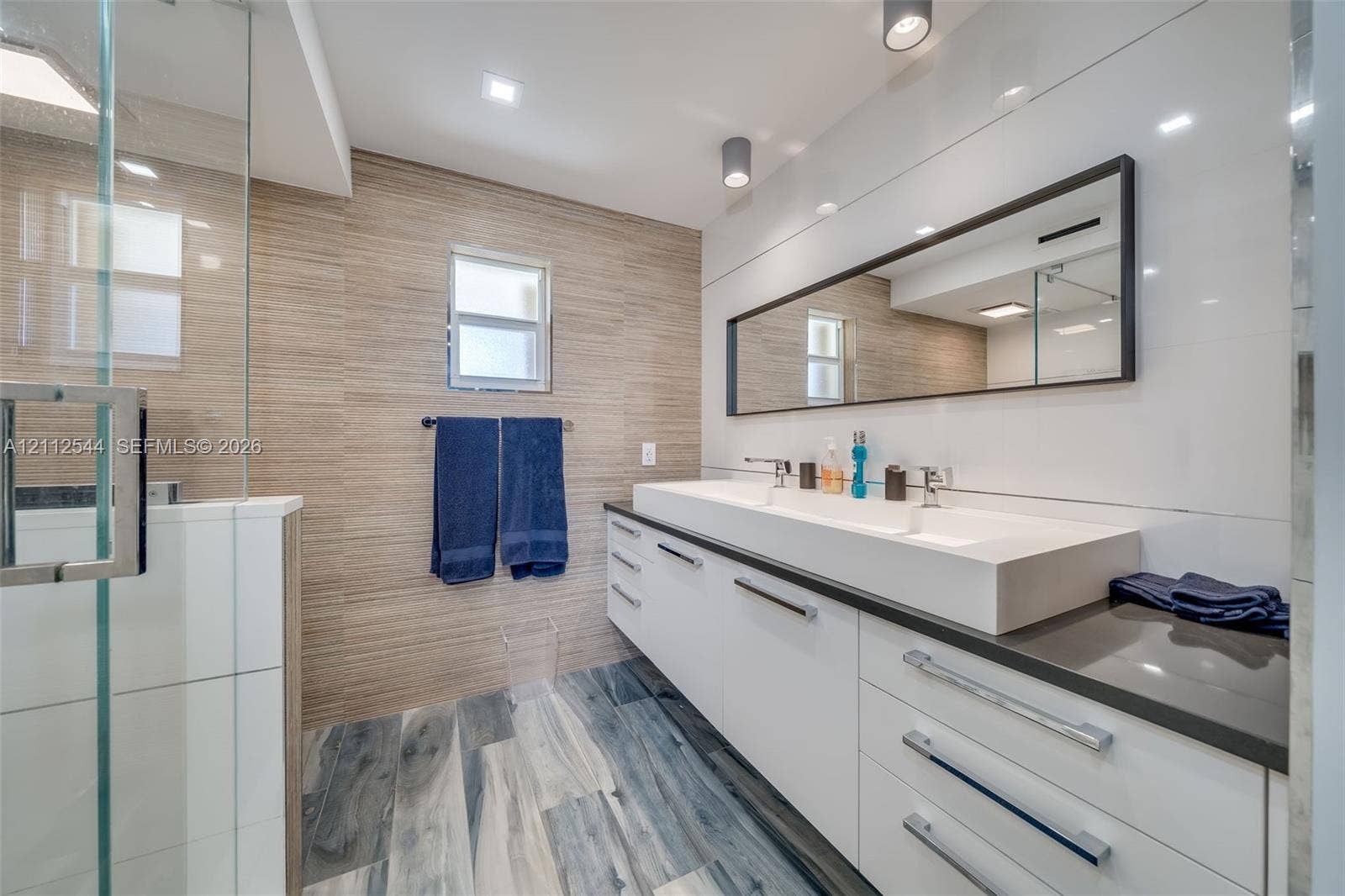 2871 N Ocean Boulevard, #R360, Boca Raton, Boca Raton, FL 33431 Bathroom featuring a floating double vanity with a rectangular sink, wood-finish flooring, a frameless glass shower enclosure, and full-width wall-mounted mirror