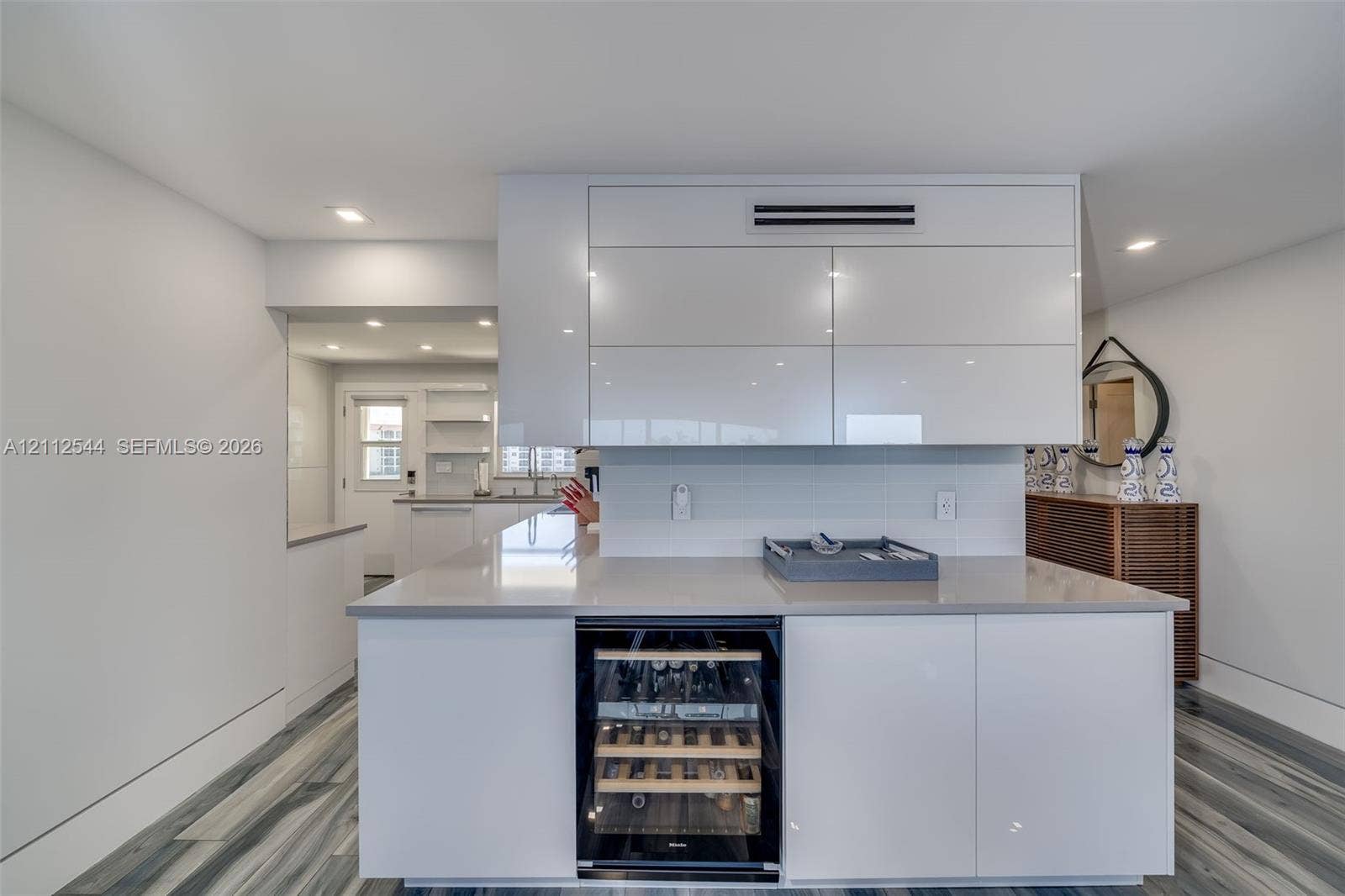 2871 N Ocean Boulevard, #R360, Boca Raton, Boca Raton, FL 33431 Kitchen island featuring high-gloss white cabinetry, integrated under-counter wine refrigerator, and stone-surface countertop, accented by wood-finish flooring and recessed lighting