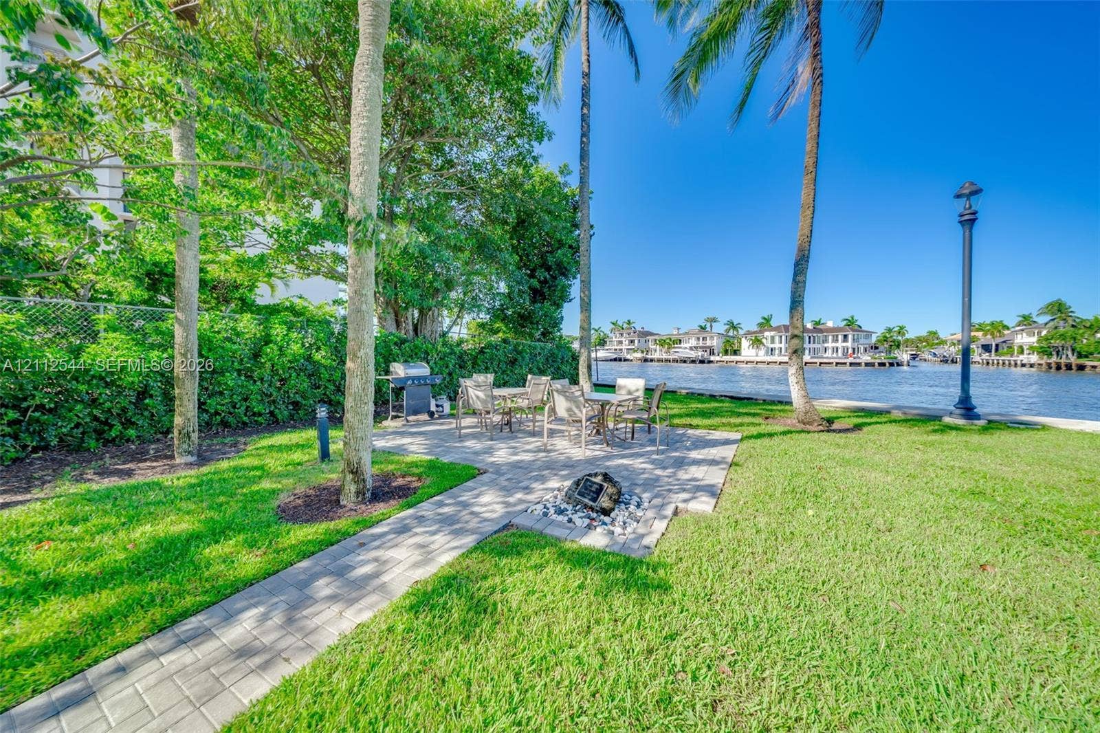 2871 N Ocean Boulevard, #R360, Boca Raton, Boca Raton, FL 33431 Waterfront grounds featuring a paver patio, manicured lawn, mature palm trees, and a decorative stone-lined fire pit area