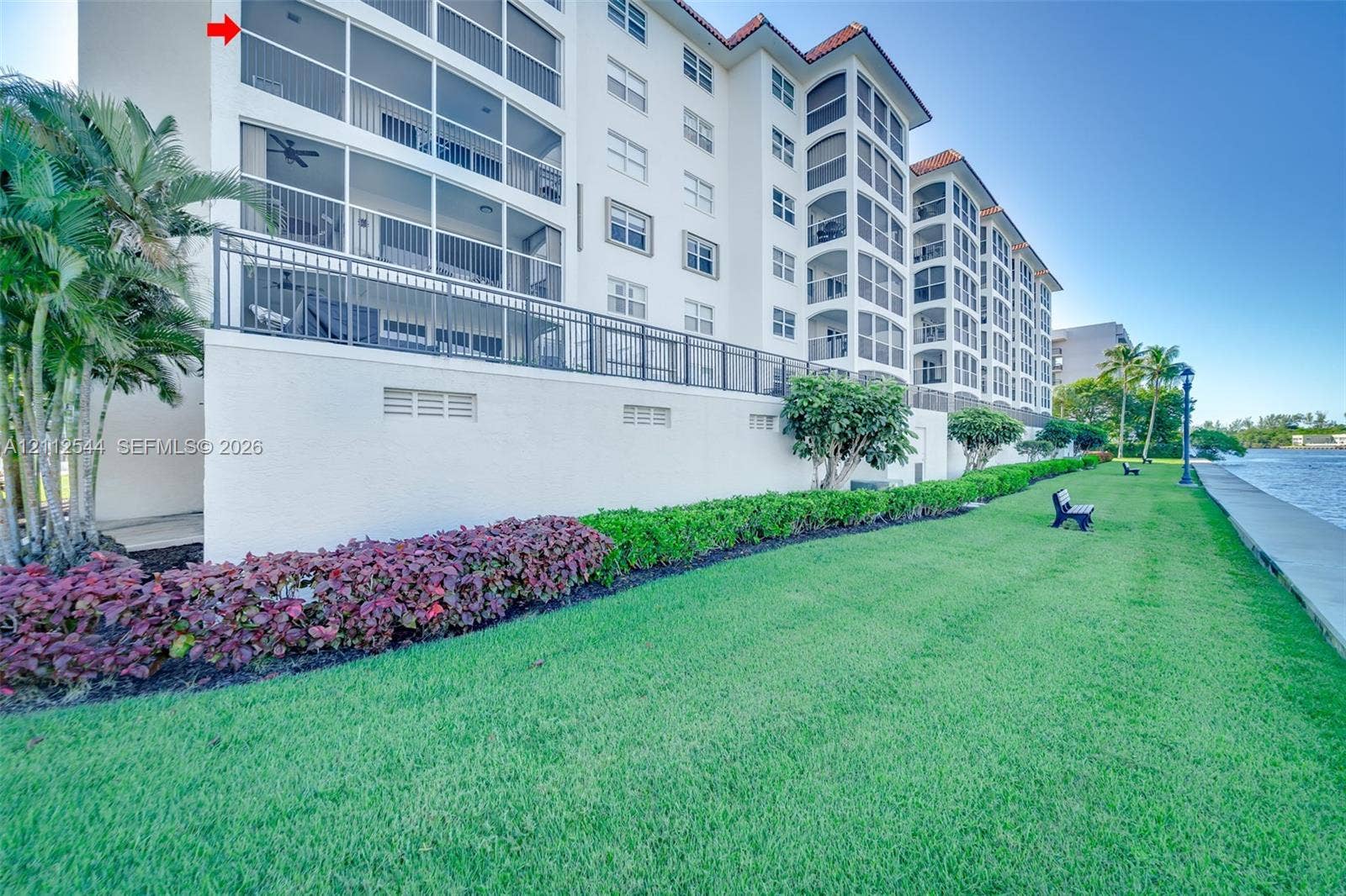 2871 N Ocean Boulevard, #R360, Boca Raton, Boca Raton, FL 33431 Multi-story building exterior featuring screened-in balconies, a stucco facade, red tile roofing, and direct waterfront grounds with manicured landscaping