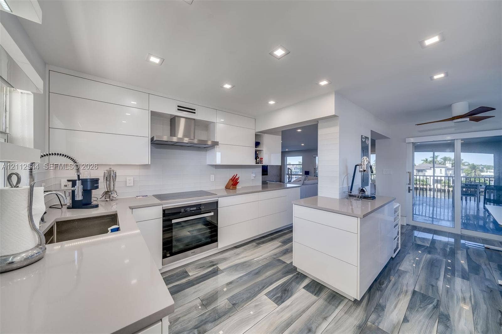 2871 N Ocean Boulevard, #R360, Boca Raton, Boca Raton, FL 33431 Modern kitchen featuring high-gloss white flat-panel cabinetry, quartz countertops, integrated stainless steel appliances, recessed ceiling lighting, and wood-finish flooring