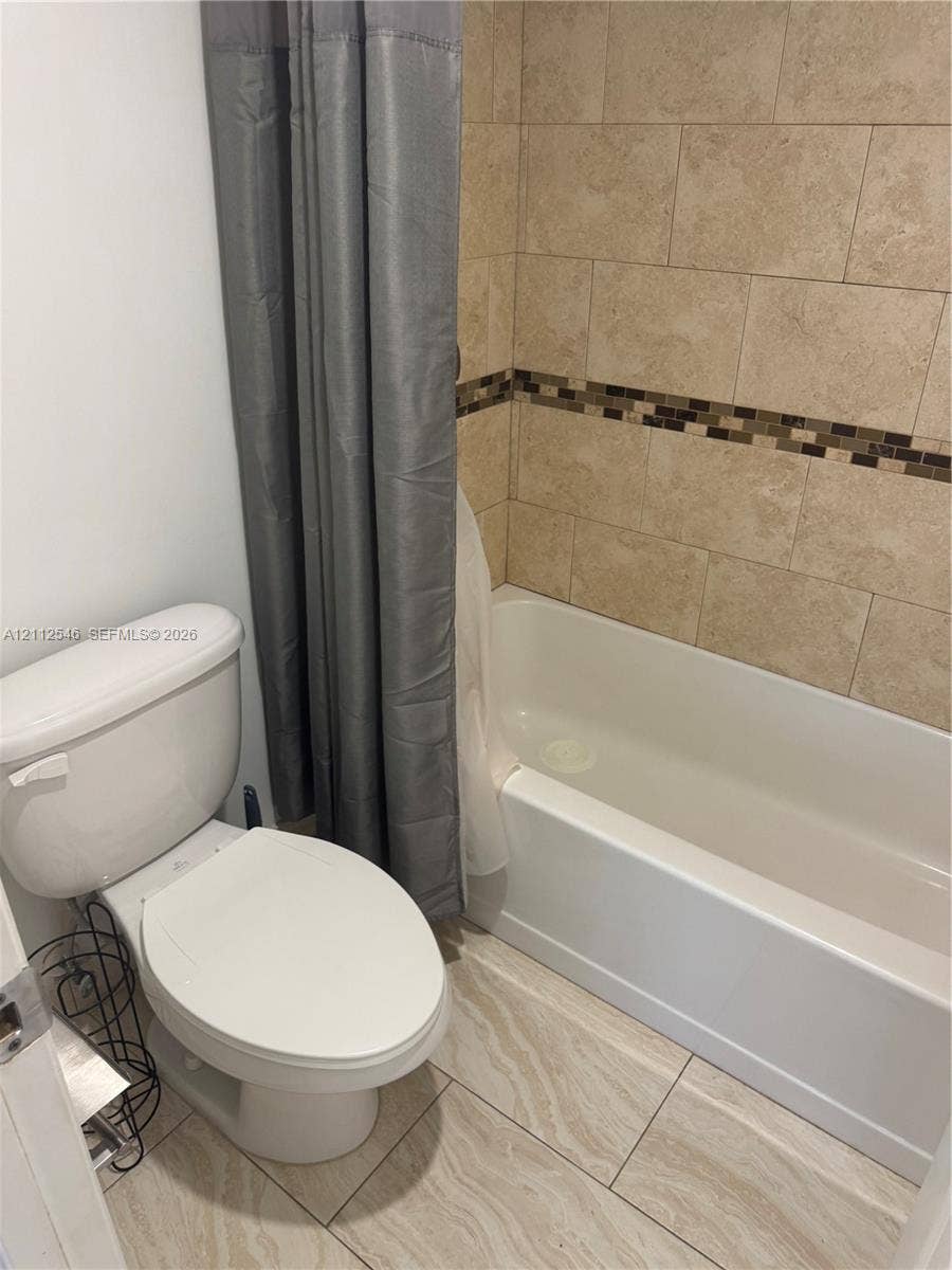 1301 NE Miami Gardens Drive, #515W, Miami, Miami, FL 33179 Bathtub with a shower surround featuring large-format stone-finish wall tiles and a decorative mosaic inlay, paired with stone-finish floor tiling