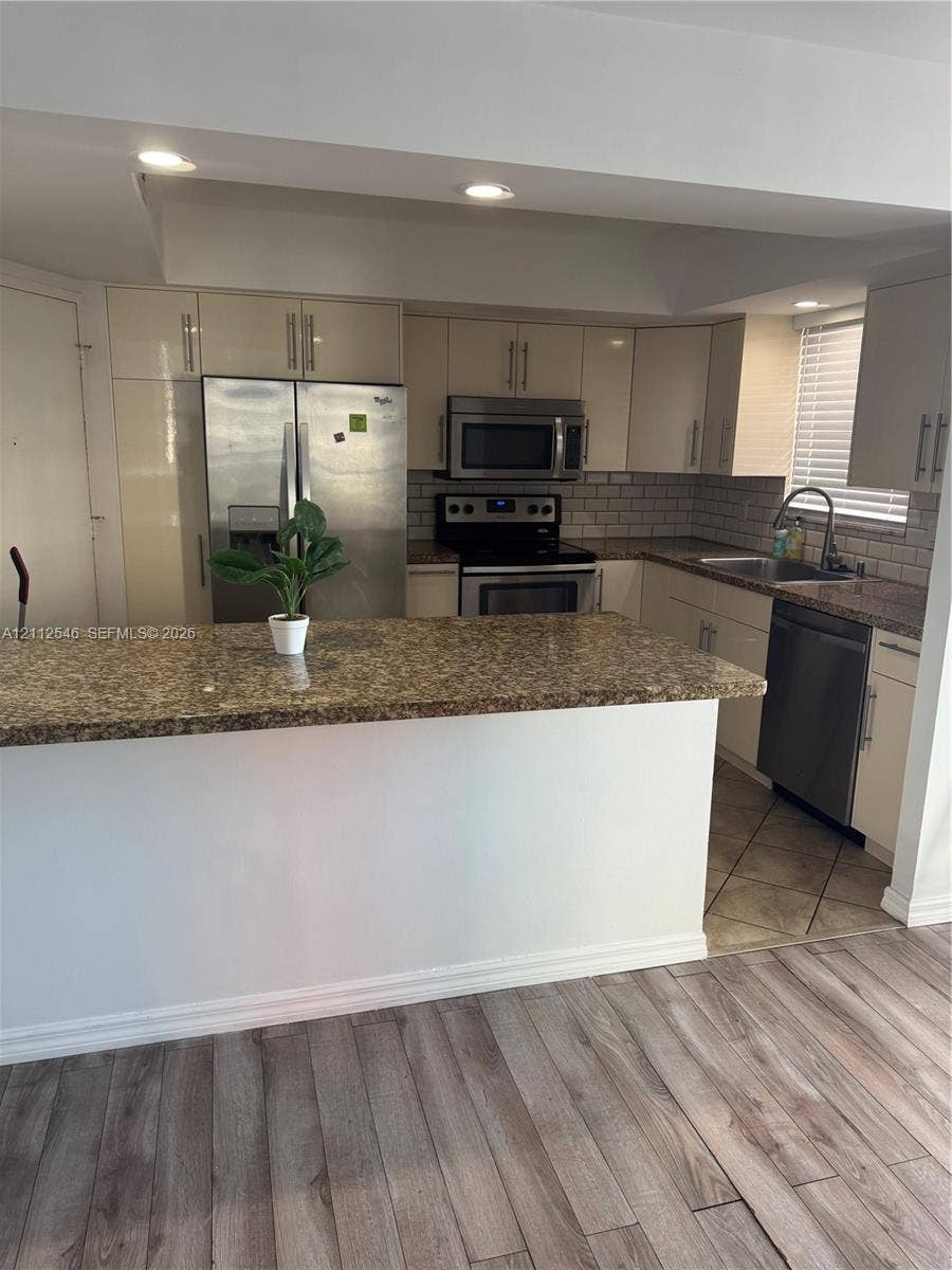 1301 NE Miami Gardens Drive, #515W, Miami, Miami, FL 33179 Kitchen featuring a breakfast bar, stone-surface countertops, subway tile backsplash, stainless steel appliances, and wood-finish flooring