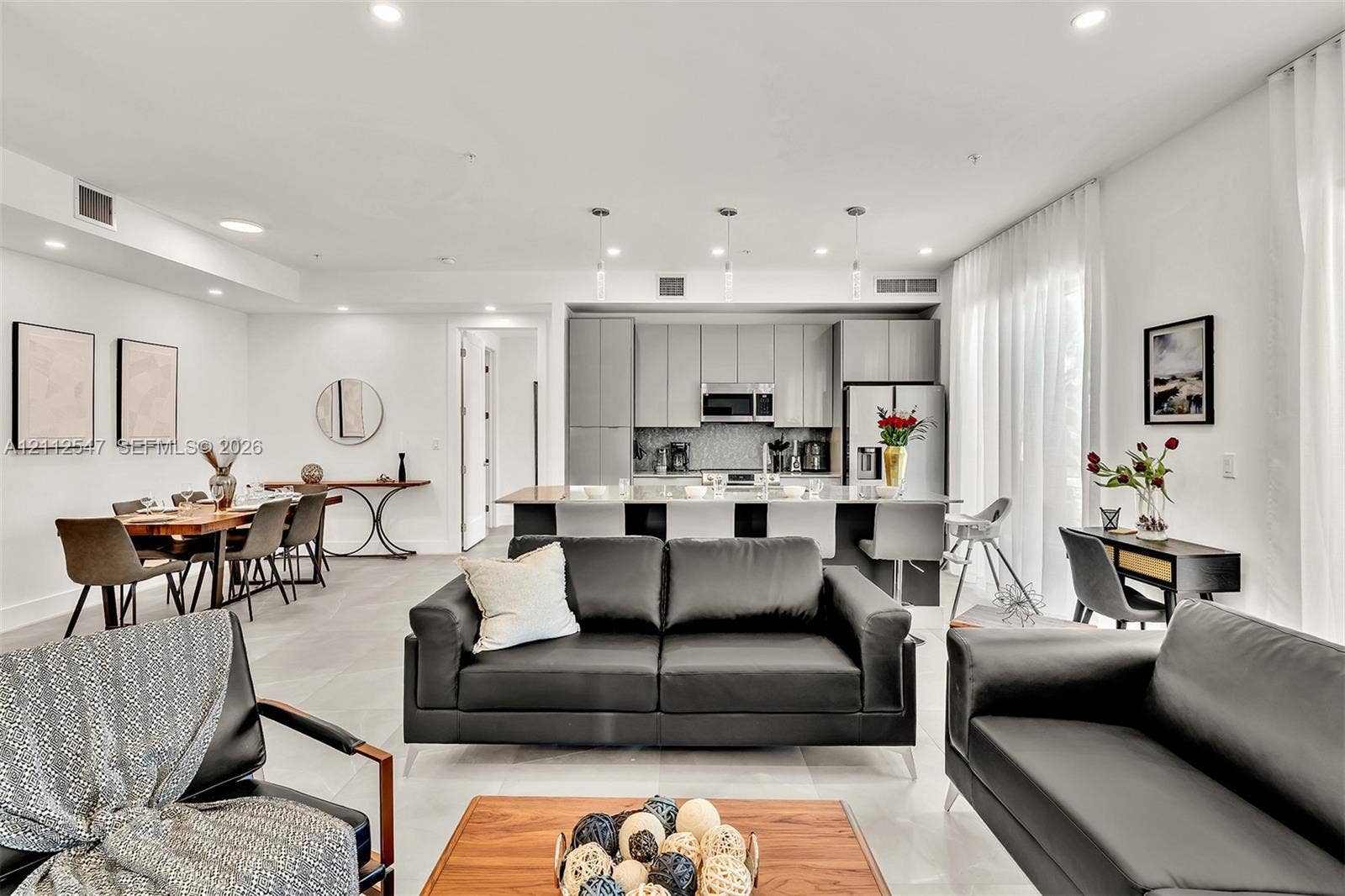 Open-concept living space featuring high-gloss cabinetry, a central kitchen island, recessed lighting, and large-format tile flooring