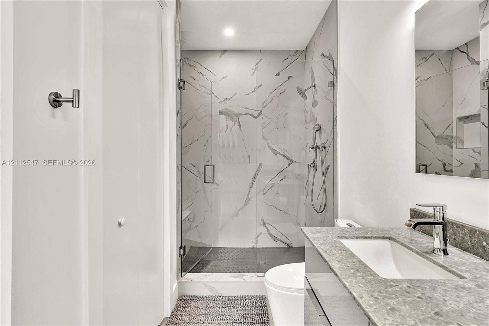 Bathroom featuring a walk-in shower with large-format stone-patterned tile, frameless glass enclosure, wall-mounted shower hardware, floating vanity with a stone countertop, and an integrated rectangular sink