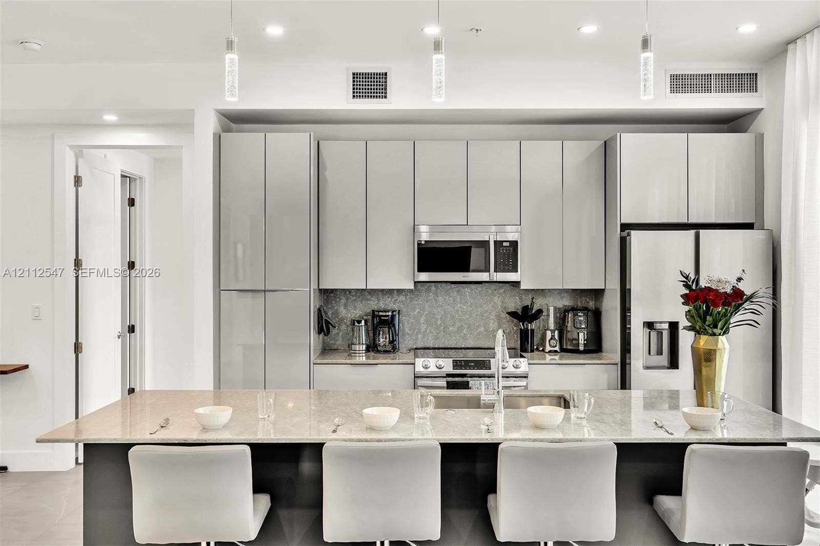 Kitchen featuring flat-panel cabinetry, a stone-surfaced kitchen island, stainless steel appliances, and glass pendant lighting