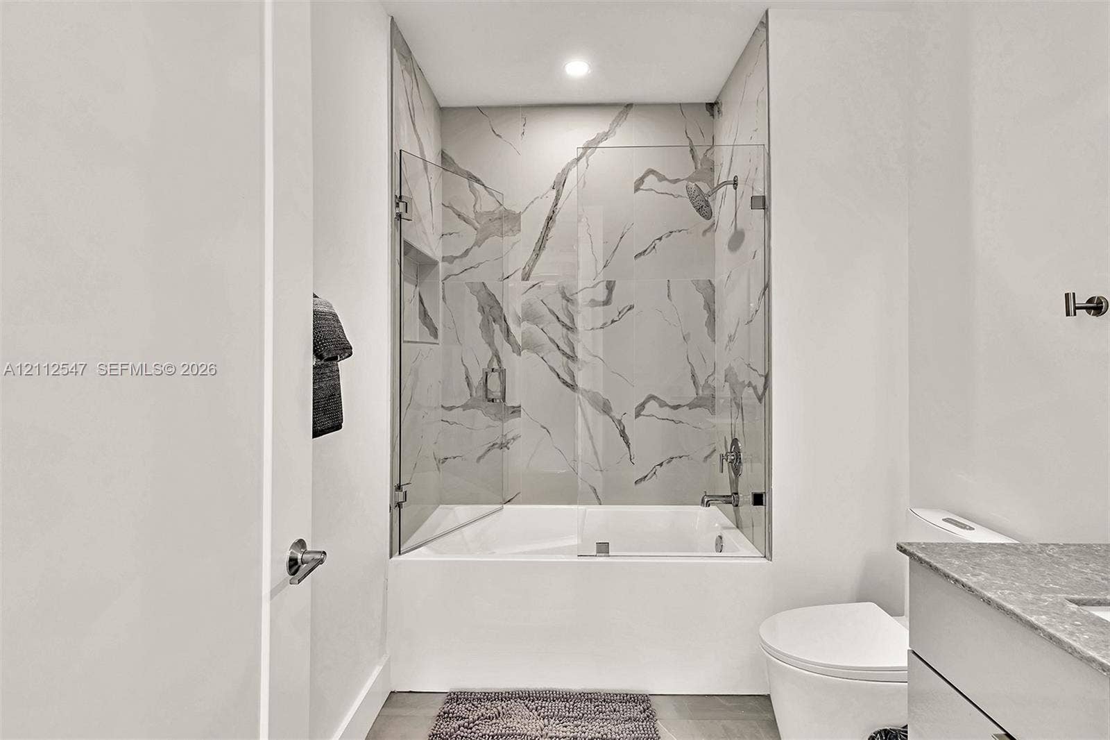Full-height shower surround with veined tile, frameless glass enclosure, recessed shower niche, deep soaking tub, and stone-finish vanity countertop