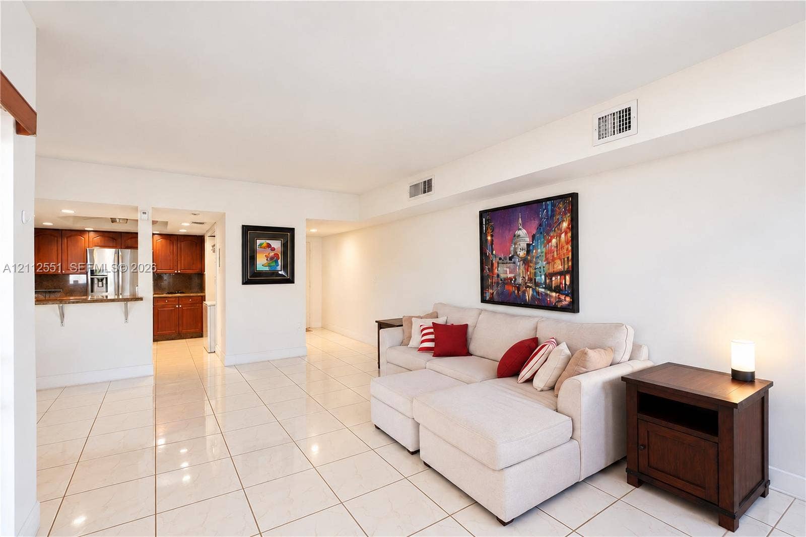 Open-concept interior featuring light-toned tile flooring, recessed ceiling lighting, and a kitchen equipped with dark wood-finish cabinetry and a breakfast bar