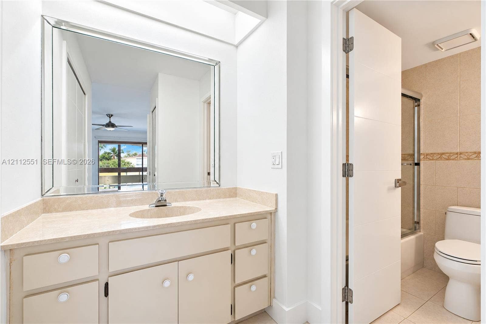 Bathroom featuring a stone-surface vanity with an integrated sink, a large beveled-edge mirror, and a tub-shower combination enclosed by a glass door