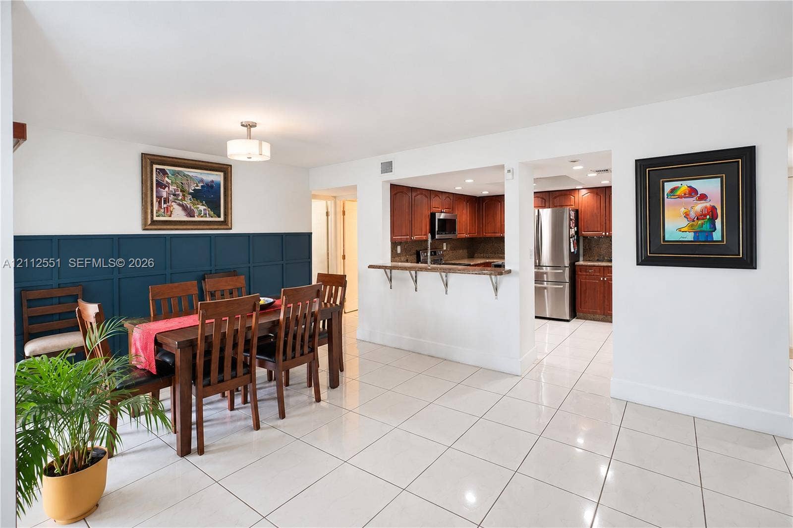 Dining area featuring wainscoting with millwork detailing, polished tile flooring, and a breakfast bar with stone-finish countertops
