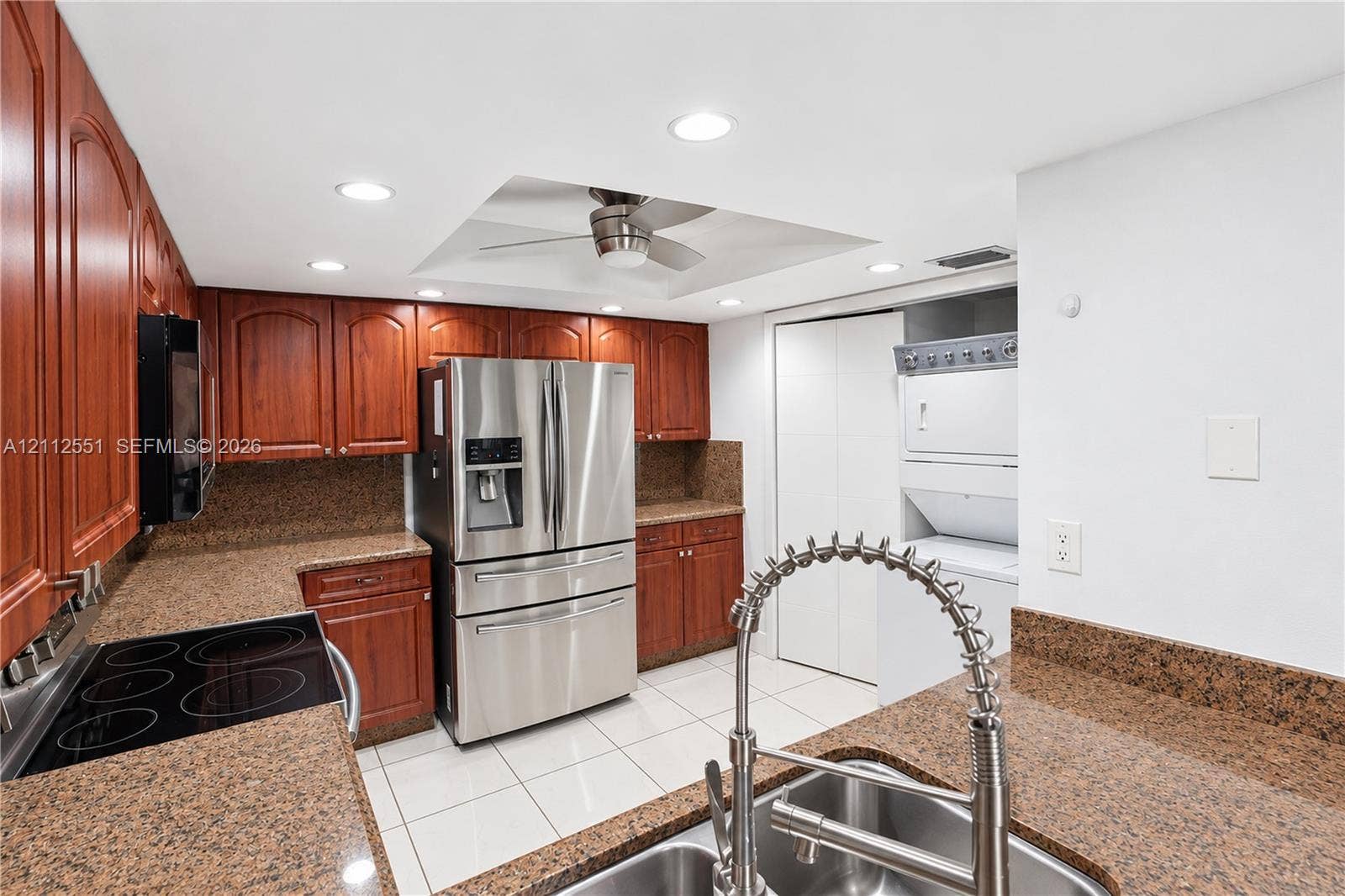 Kitchen featuring stained-wood cabinetry, stone-finish countertops, stainless steel appliances, recessed ceiling lighting, and a stackable laundry unit enclosed in a closet