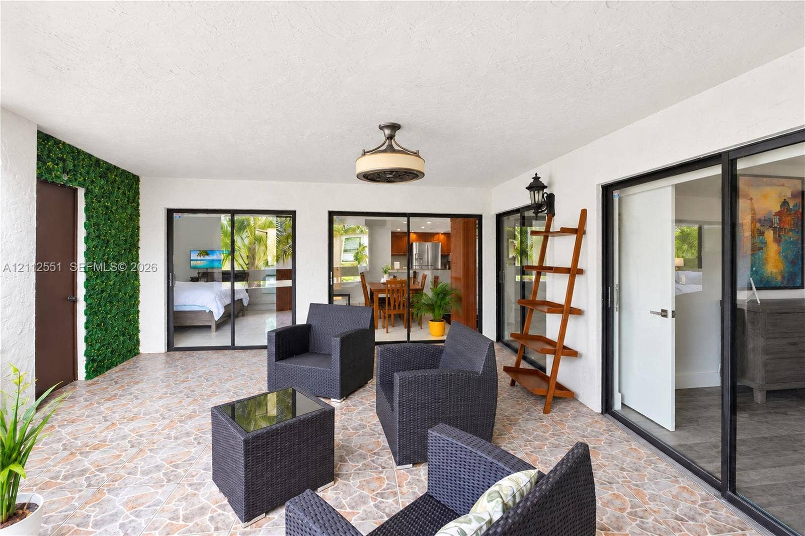 Covered patio featuring stone-tile flooring, decorative green wall accent, ceiling-mounted light fixture, and multiple sliding glass door entries