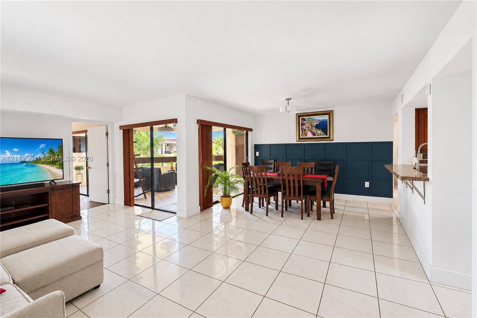 Large format ceramic tile flooring, dual sliding glass doors, and a deep-blue grid wainscoting accent wall, complemented by a kitchen pass-through counter