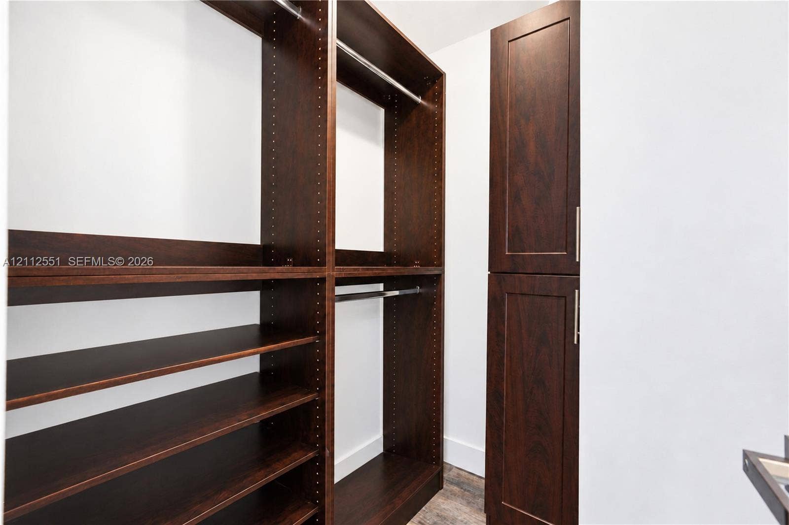 Built-in dark wood-finish cabinetry featuring adjustable shelving, integrated hanging rods, and full-height cabinetry with metallic hardware
