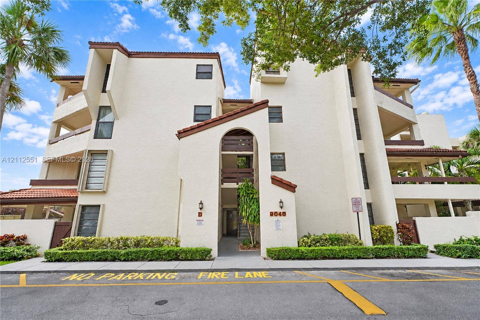 Multi-story stucco exterior featuring arched entryway detailing, tiled roof accents, integrated private balconies, and manicured landscaping