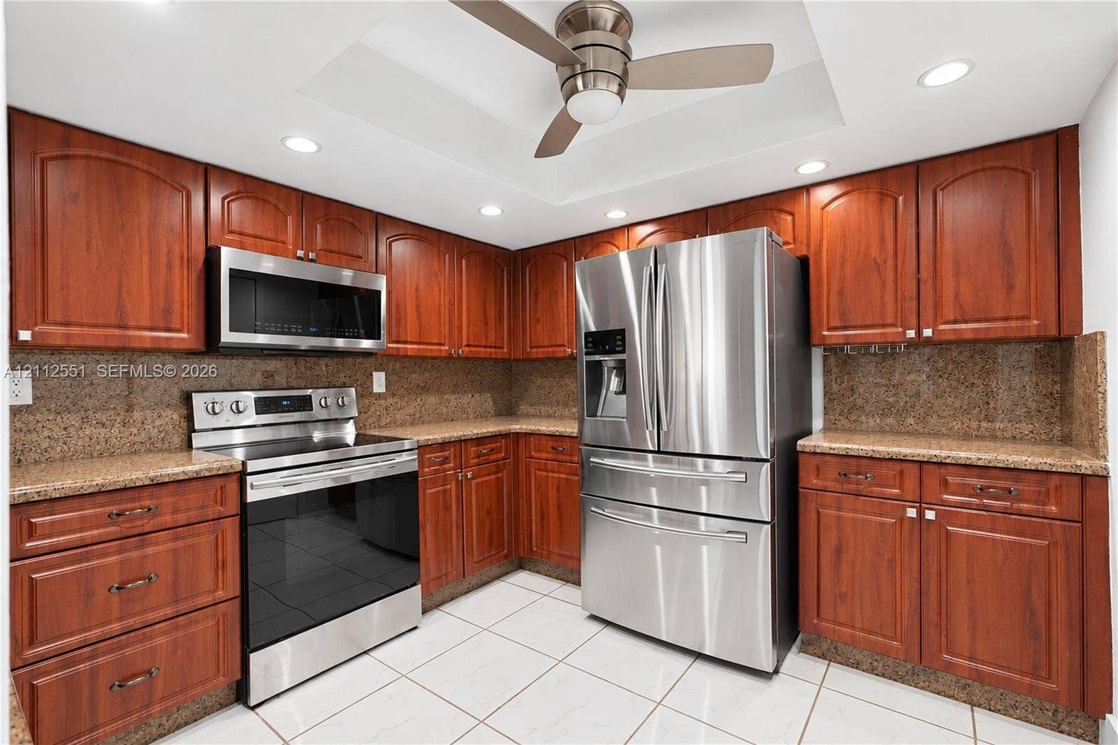 Kitchen featuring cherry-finish cabinetry, stone countertops, stainless steel appliances, a recessed ceiling with a central fan, and tile flooring