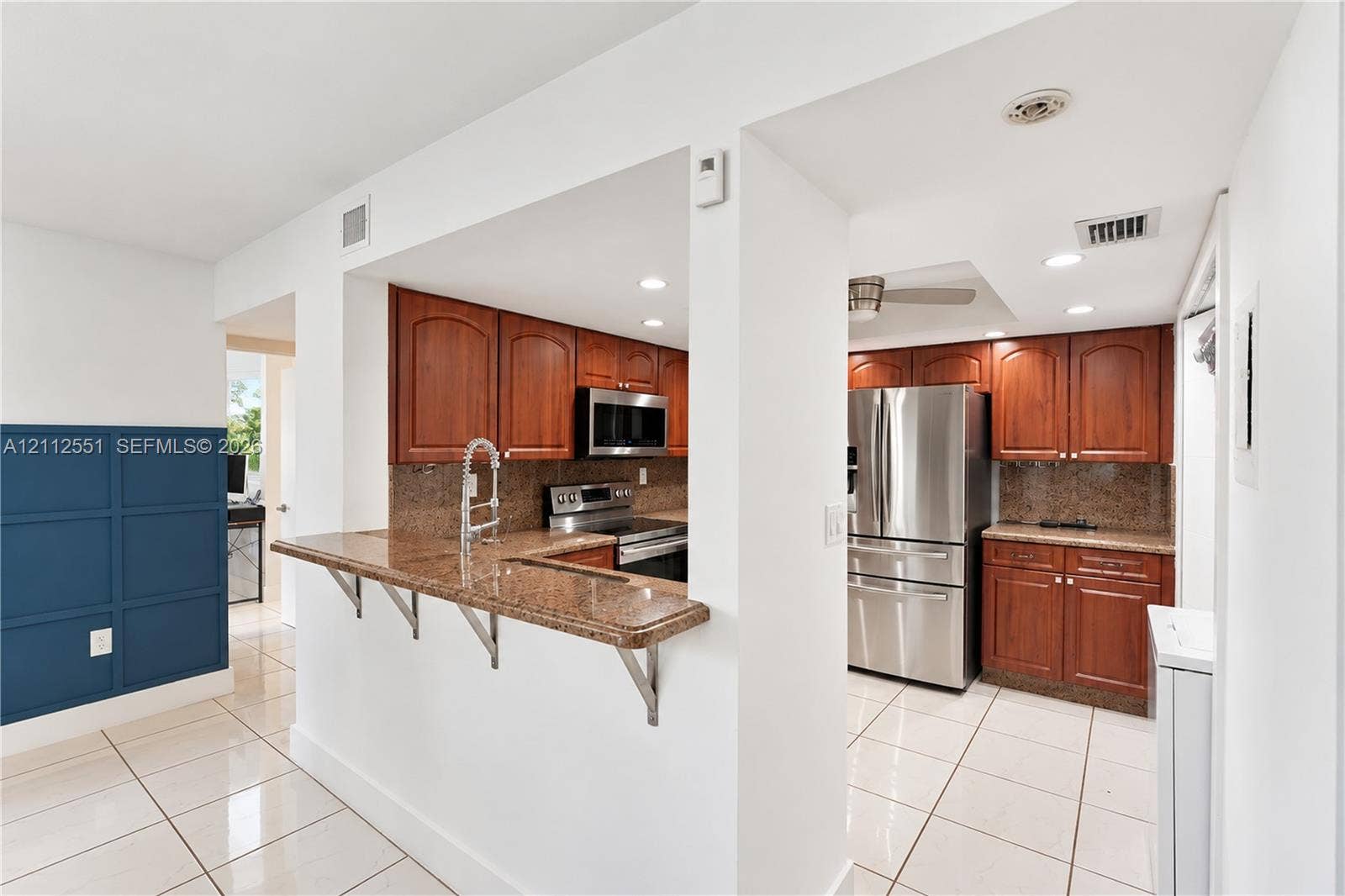 Kitchen featuring stained wood cabinetry, stone-surface countertops, breakfast bar, and stainless steel appliances, accented by tile flooring and blue paneled wall detailing