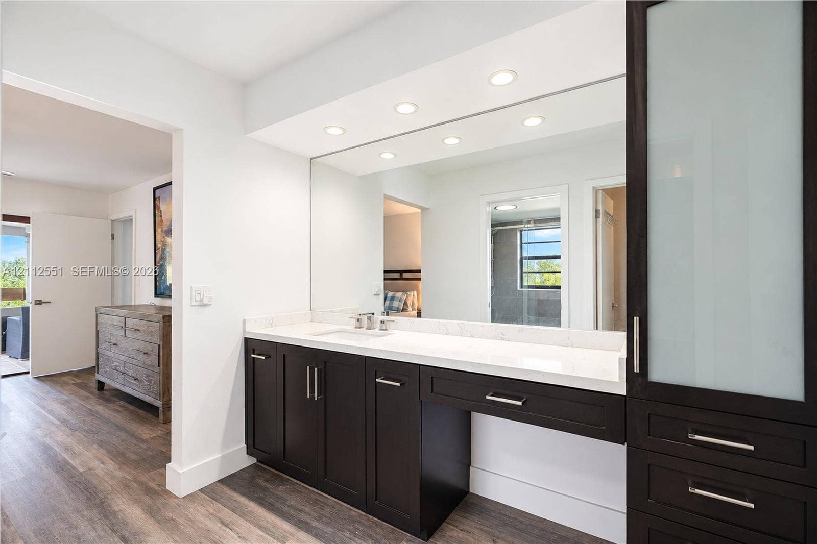 Vanity featuring dark cabinetry, stone-finish countertop, under-mount sink, integrated full-width mirror, and tall frosted-glass linen storage