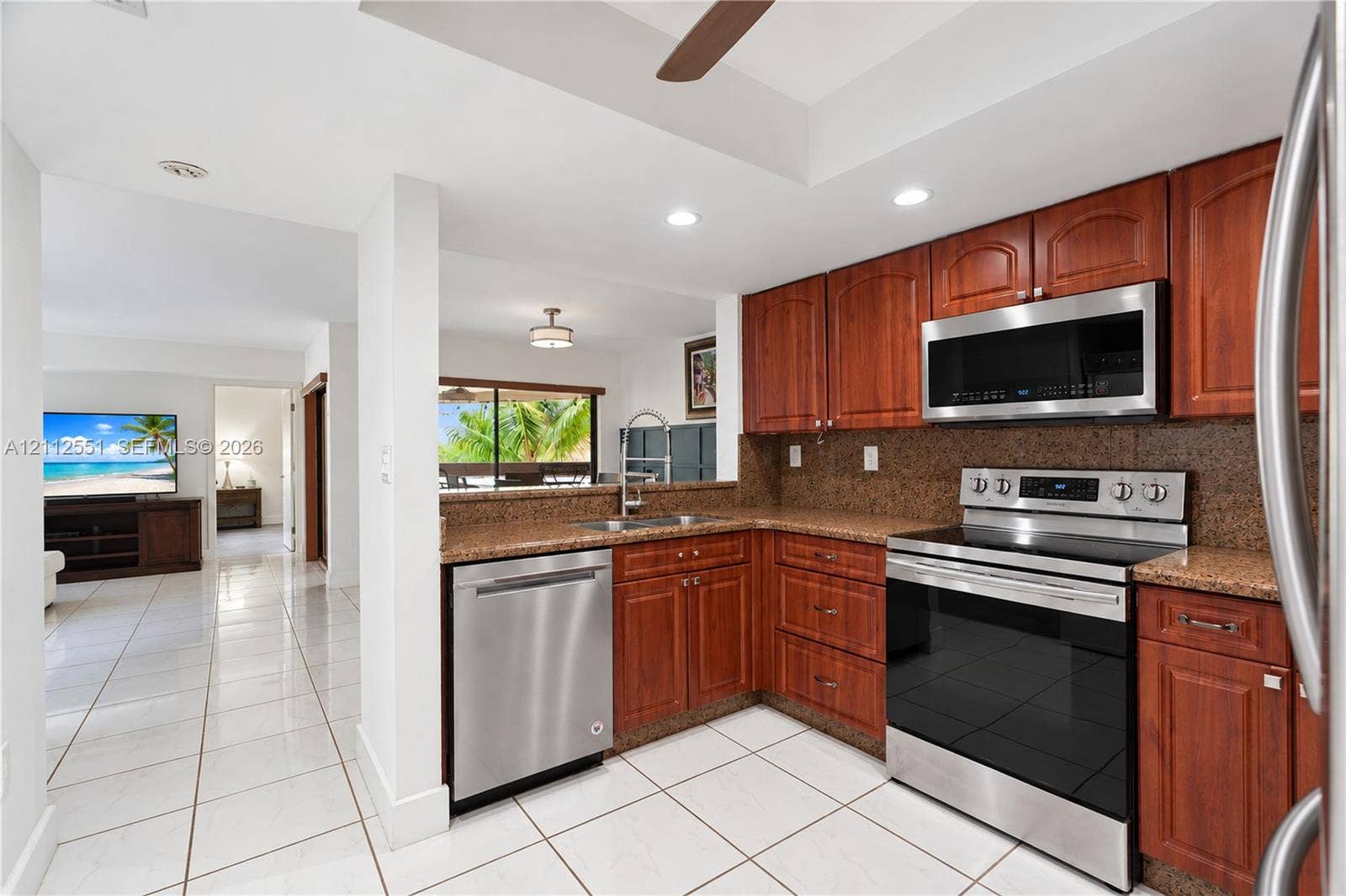Kitchen featuring cherry-finish cabinetry, stone-texture countertops, stainless steel appliances, and tile flooring