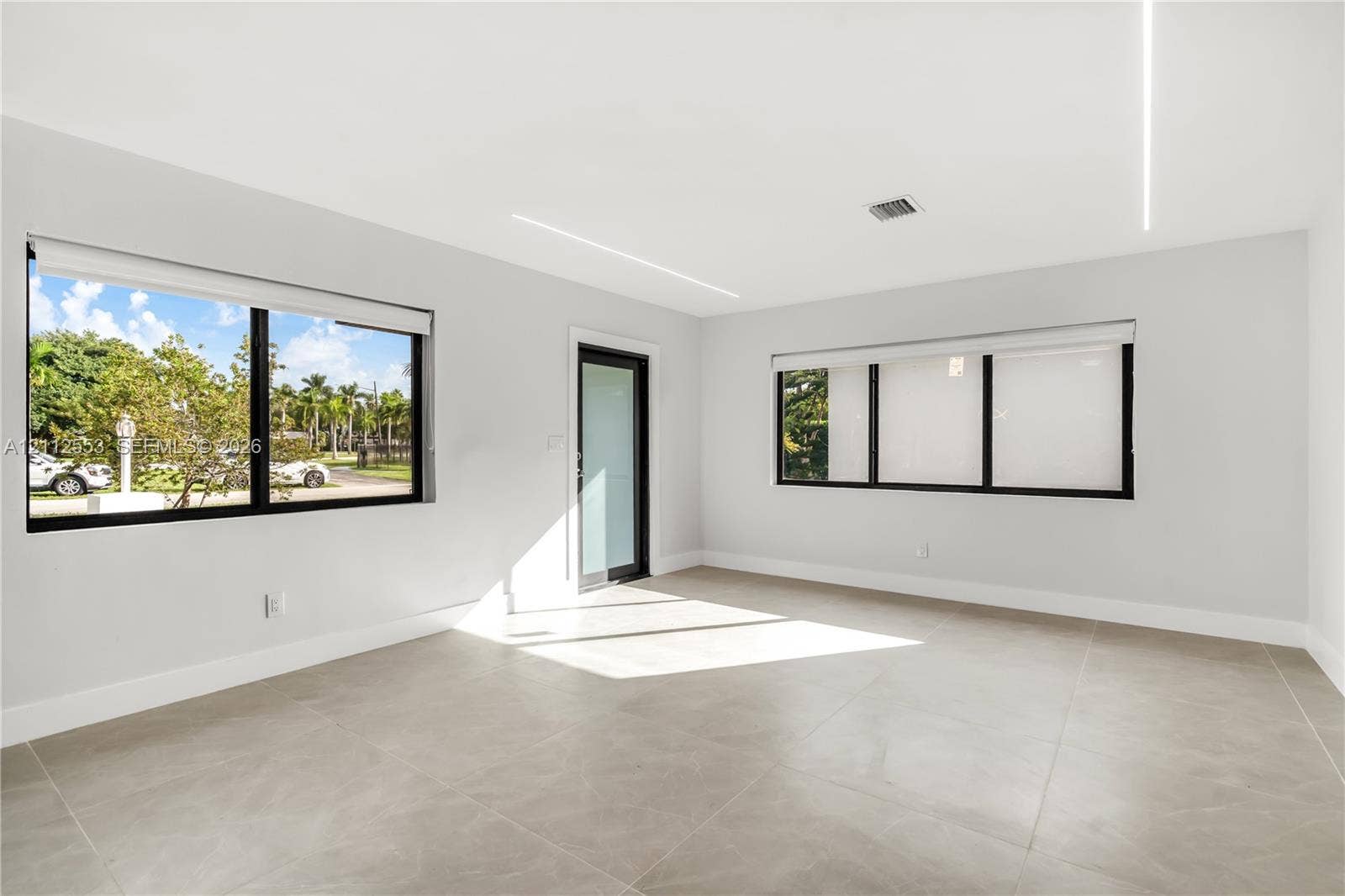 Interior space featuring large-format tile flooring, recessed linear ceiling lighting, black-framed windows with integrated shades, and a glass-paneled exterior door
