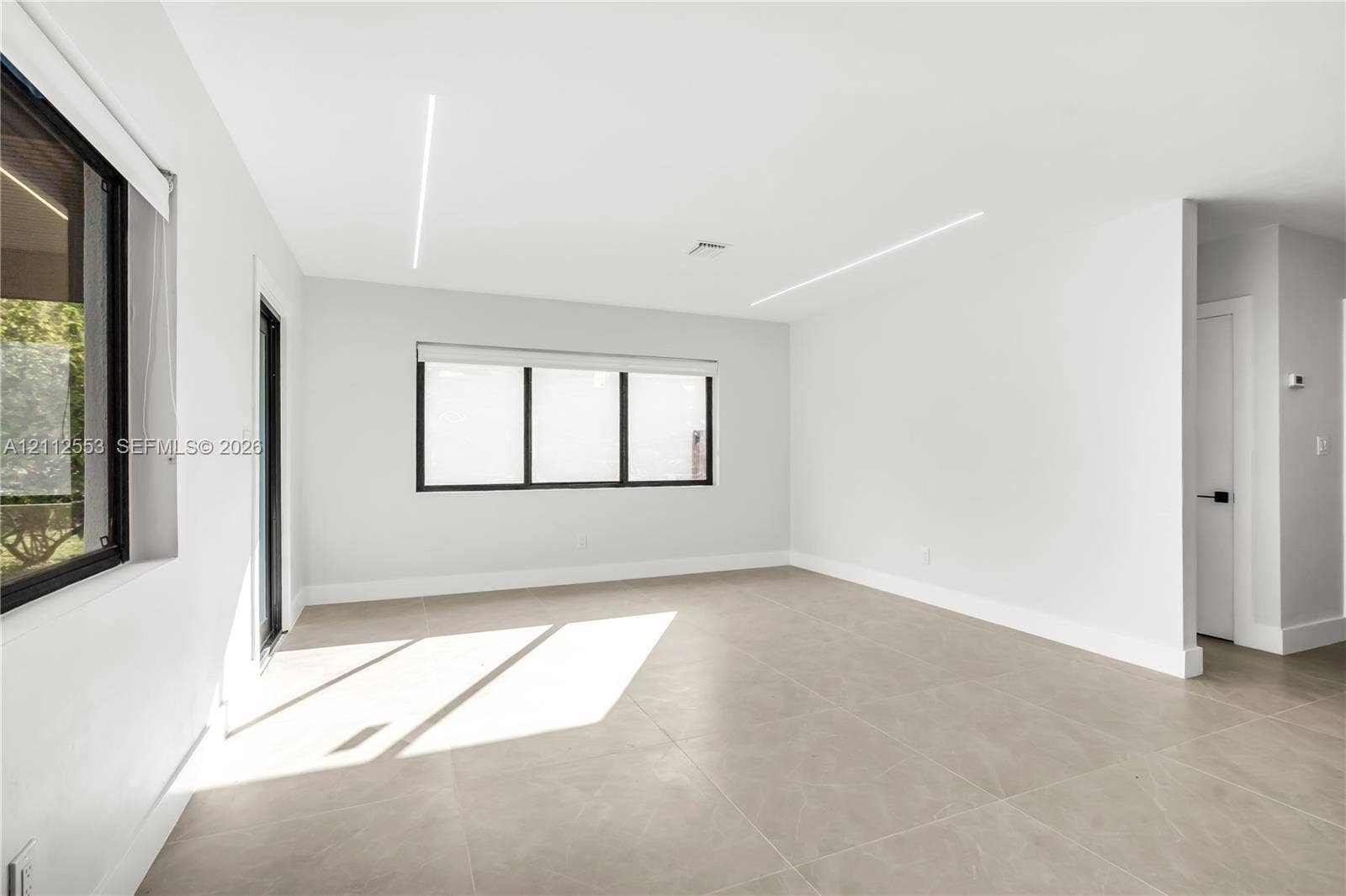 Neutral-toned tile flooring, recessed linear LED ceiling lighting, and black-framed windows