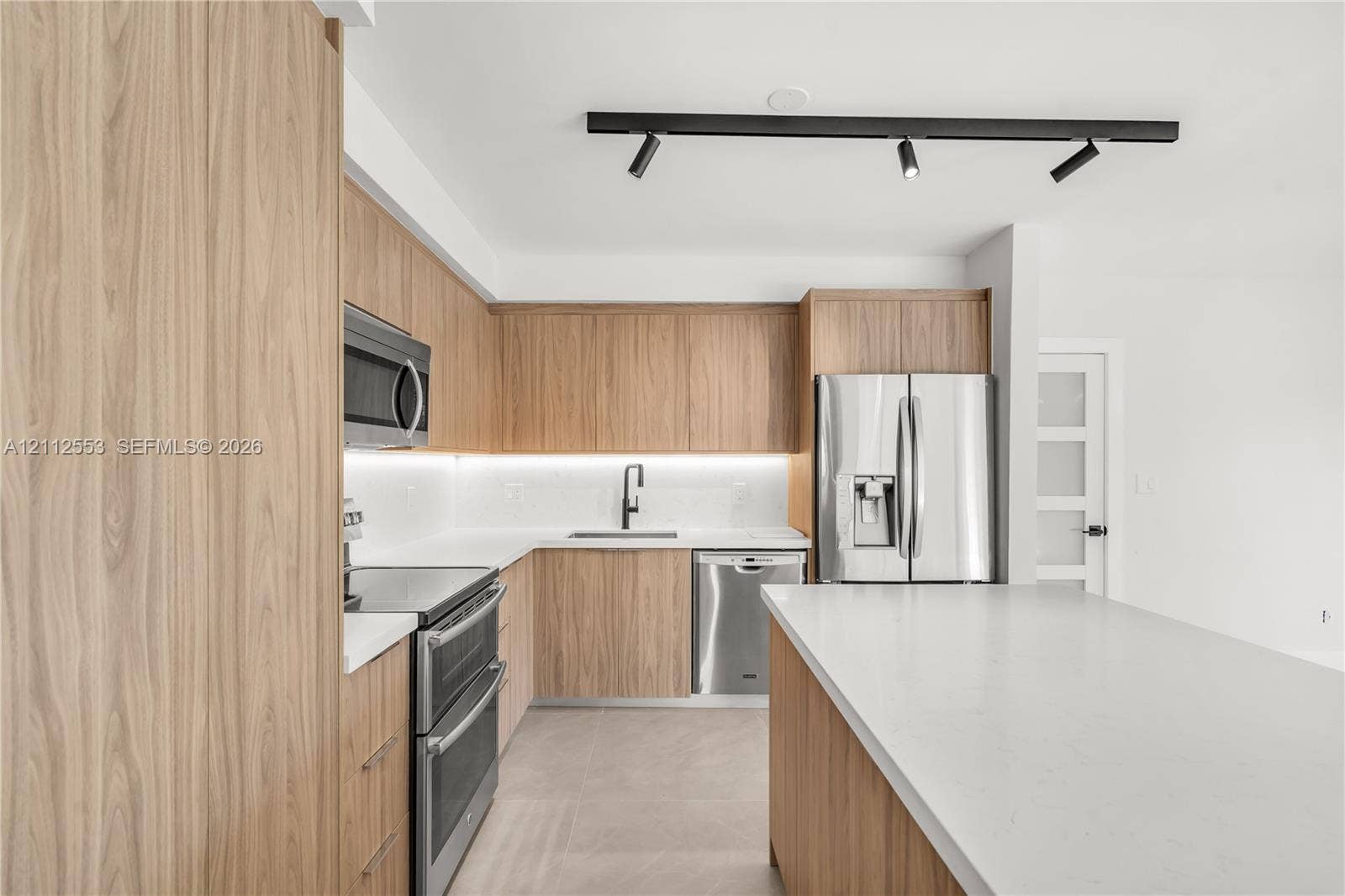 Kitchen featuring wood-finish cabinetry, quartz countertops, stainless steel appliances, under-cabinet lighting, and track lighting